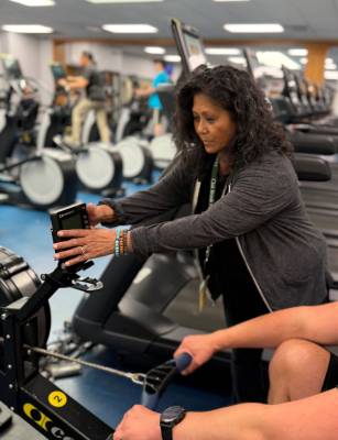 Personal trainer assisting a client on a rowing machine during a session. 