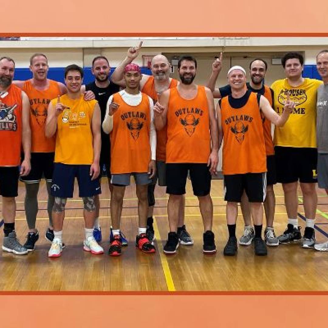 Adult basketball team posing together on a gym court during a recreational league game.